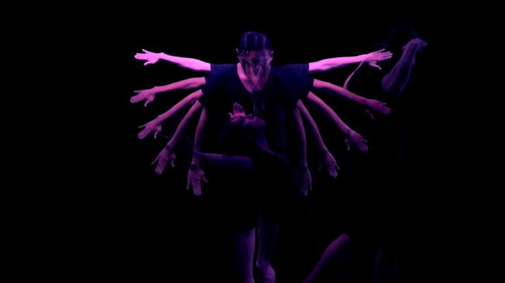 Using a mirror tool, this still uses a mirror symmetry effect on top of footage of a person dancing. They have their left hand placed over their heart and their right arm draped over their face. The setting is very dark with atmospheric blue toned lighting. A pale full moon is positioned in the center of the frame where the mirror symmetry line stands.