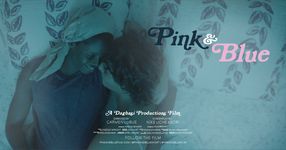 Two people cuddling in bed. The one on the left has dark brown skin with a tan head wrap and a blue tank top. The one on the right has light skin with short curly hair and a white tank top. The title is displayed on the right-hand side saying "Pink & Blue". Pink is in blue font and blue is written in pink font.