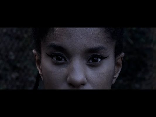 It's a shot of someone's face from the nose to forehead. They have light brown skin and their hair pulled back. They are wearing black eyeliner and in front of a blurred background.