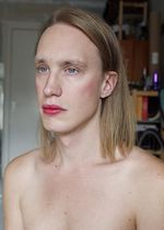 An intimate and artistic self-portrait of Ester Martin Bergsmark from the shoulders and above, photographed at home in daylight. Ester has fair skin, dark blonde collarbone-length hair, and blue eyes. She has light makeup and is posed in a quarter turn from the camera and gazing in the same direction.