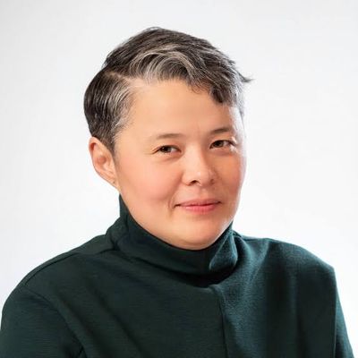 Professional portrait of Elisha Lim from the shoulders and above, taken in front of a bright white backdrop. Elisha has light tan skin, brown eyes, and dark hair with some silver-gray strands towards the front. They are wearing a dark turtleneck.