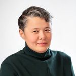 Professional portrait of Elisha Lim from the shoulders and above, taken in front of a bright white backdrop. Elisha has light tan skin, brown eyes, and dark hair with some silver-gray strands towards the front. They are wearing a dark turtleneck.