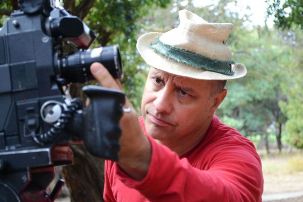 Brian Favorite adjusts the focus on a camera lens. He has a look of concentration, light skin and short hair which peeks out from under a straw fedora.