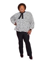 Jonathan P. Higgins is a nonbinary Black person with brown skin. They are wearing a black and white polka dot blouse, black pants and a black ascot. They have short curly brown hair posing with their left hand on their hip.

