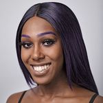 Ahya Simone is a Black trans woman with dark brown skin posed in front of a gray background. She has long straight purple hair and purple eyebrows.