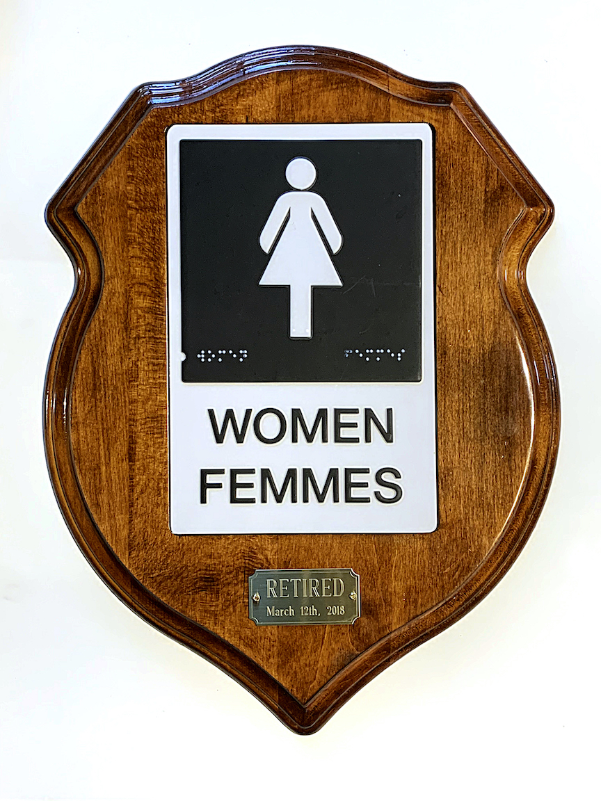 A women's bathroom sign mounted like a trophy with the label "RETIRED."