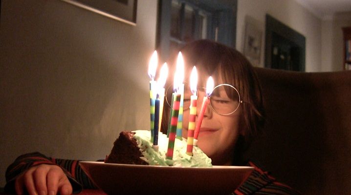 white child smiling with eyes closed behind lit birthday cake