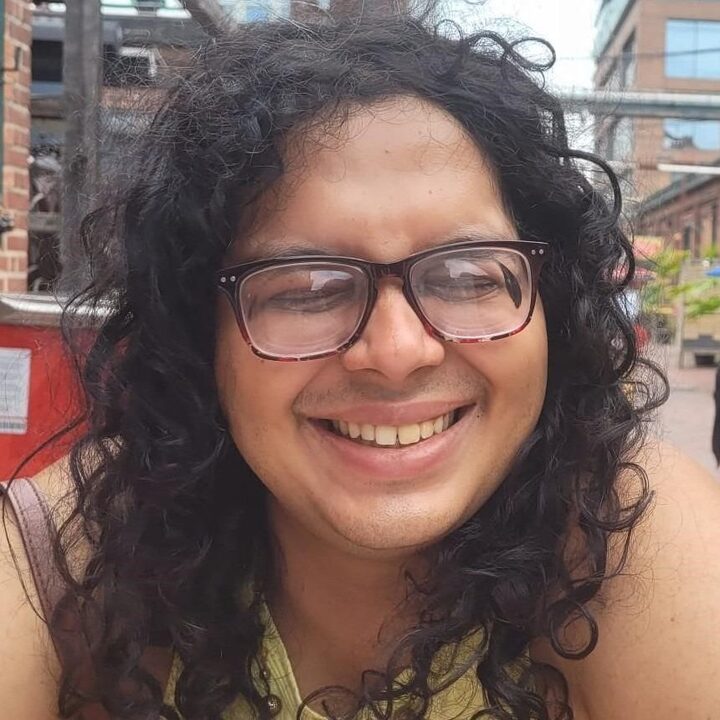 Rohan Faiyaz Khan pictured with long curly hair and wearing glasses smiling widely.